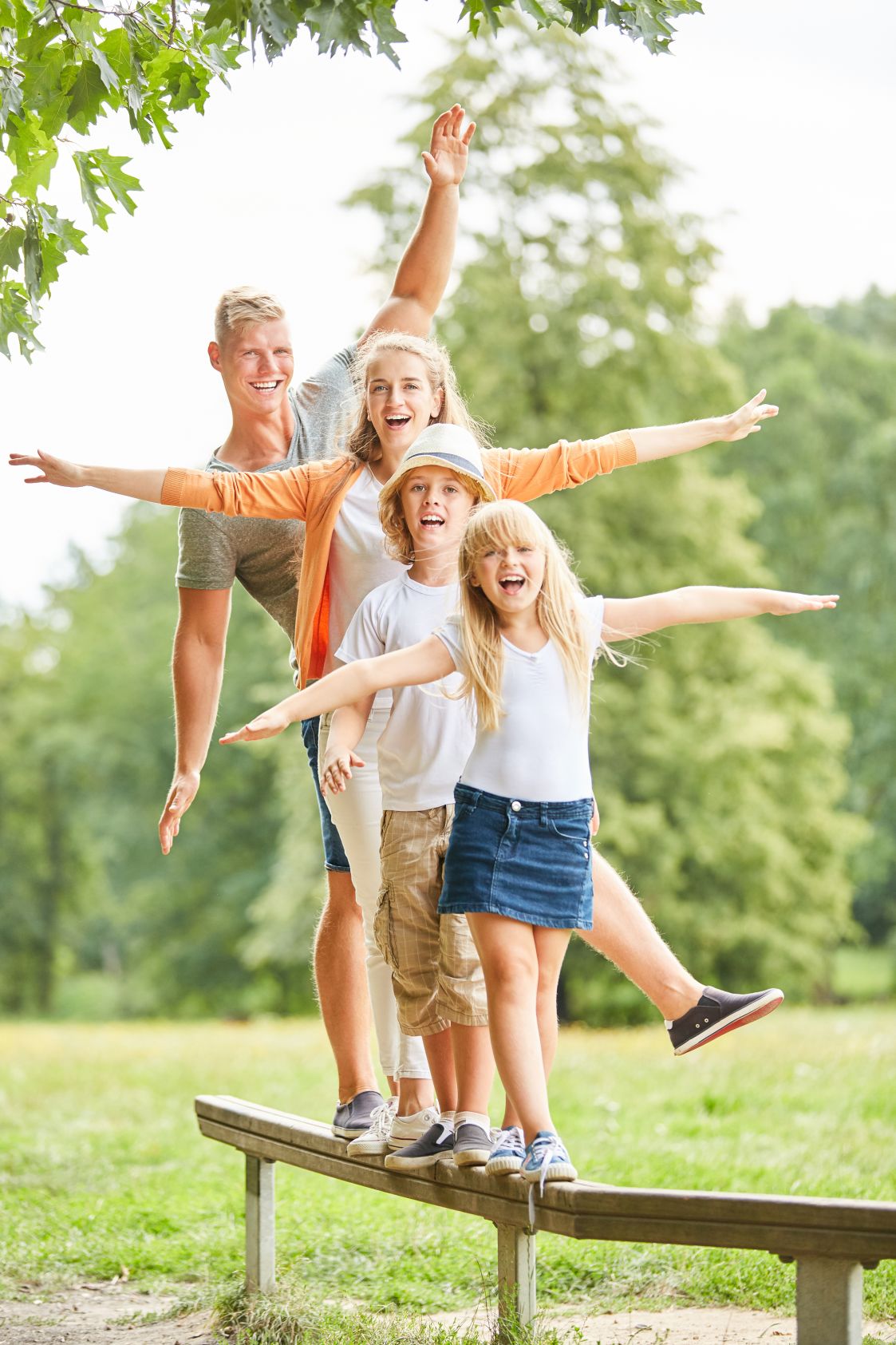 Familie und Kinder machen eine Balance Übung auf dem Trimm dich Pfad