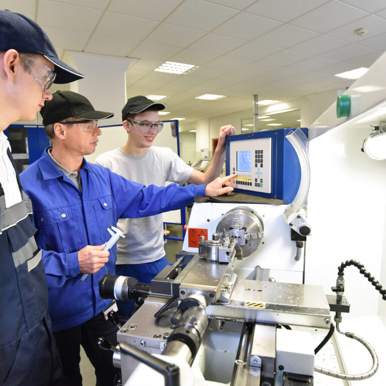 young apprentices in technical vocational training are taught by older trainers on a cnc lathes machine