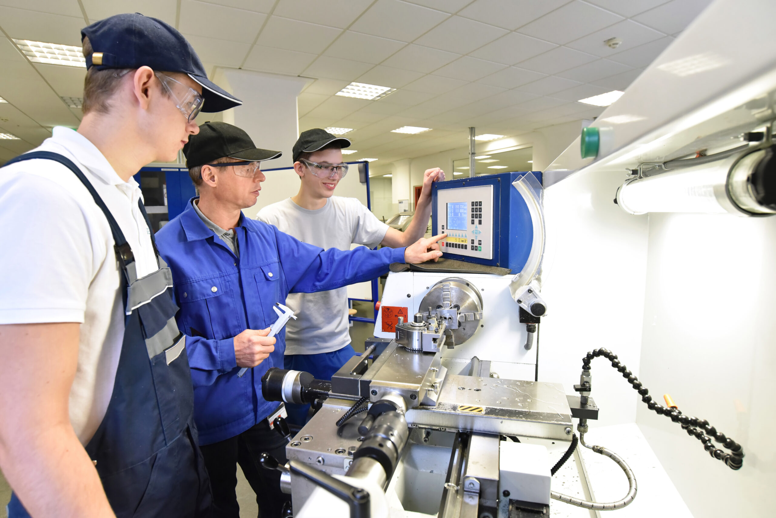 young apprentices in technical vocational training are taught by older trainers on a cnc lathes machine