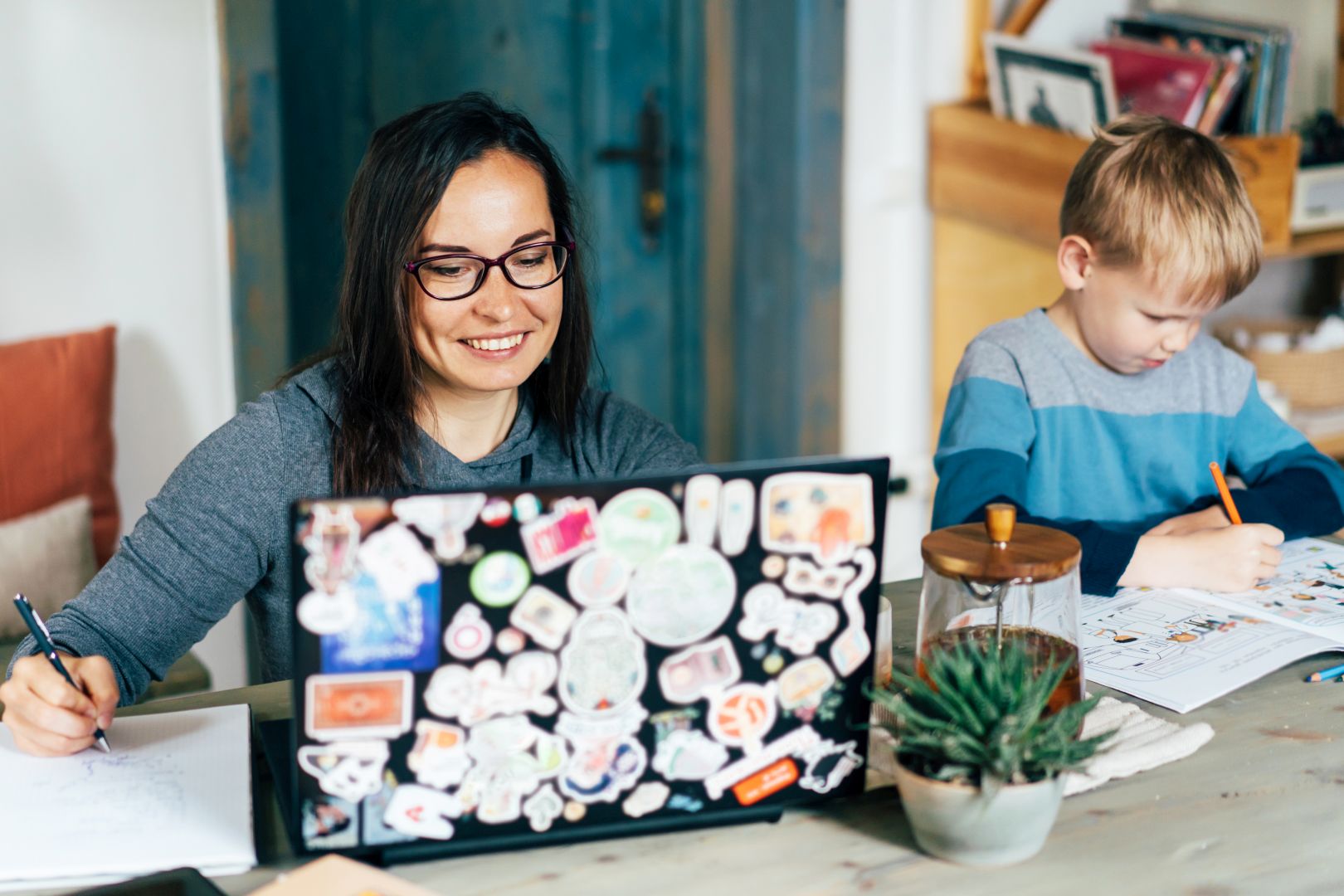 Work from home and family education. Mom and son are sitting at the desk. Business woman works in a laptop, a child writes in a textbook. Remote access using technology. Self-isolation and quarantine.