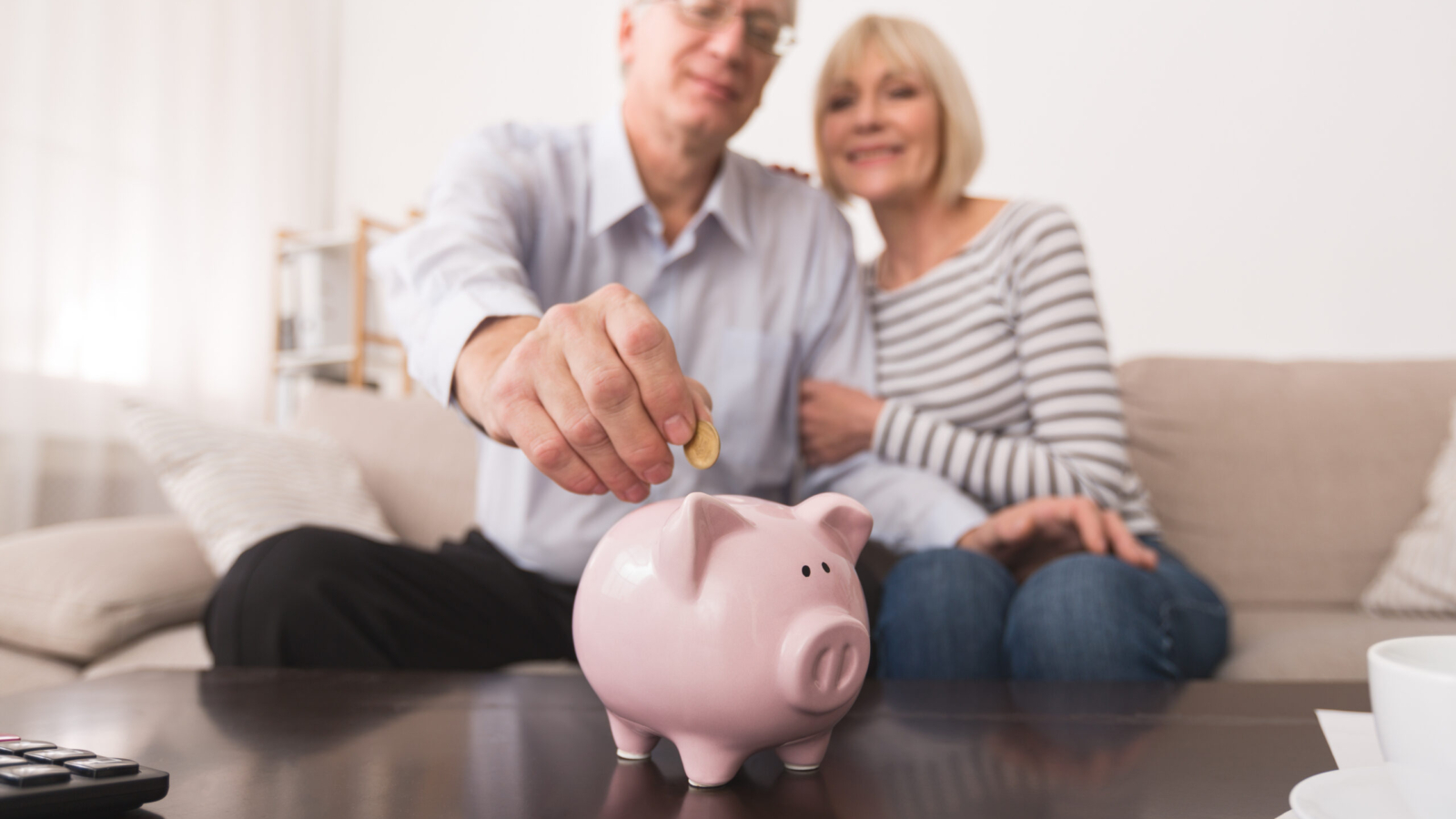 Senior couple putting coin in piggybank, saving money at home