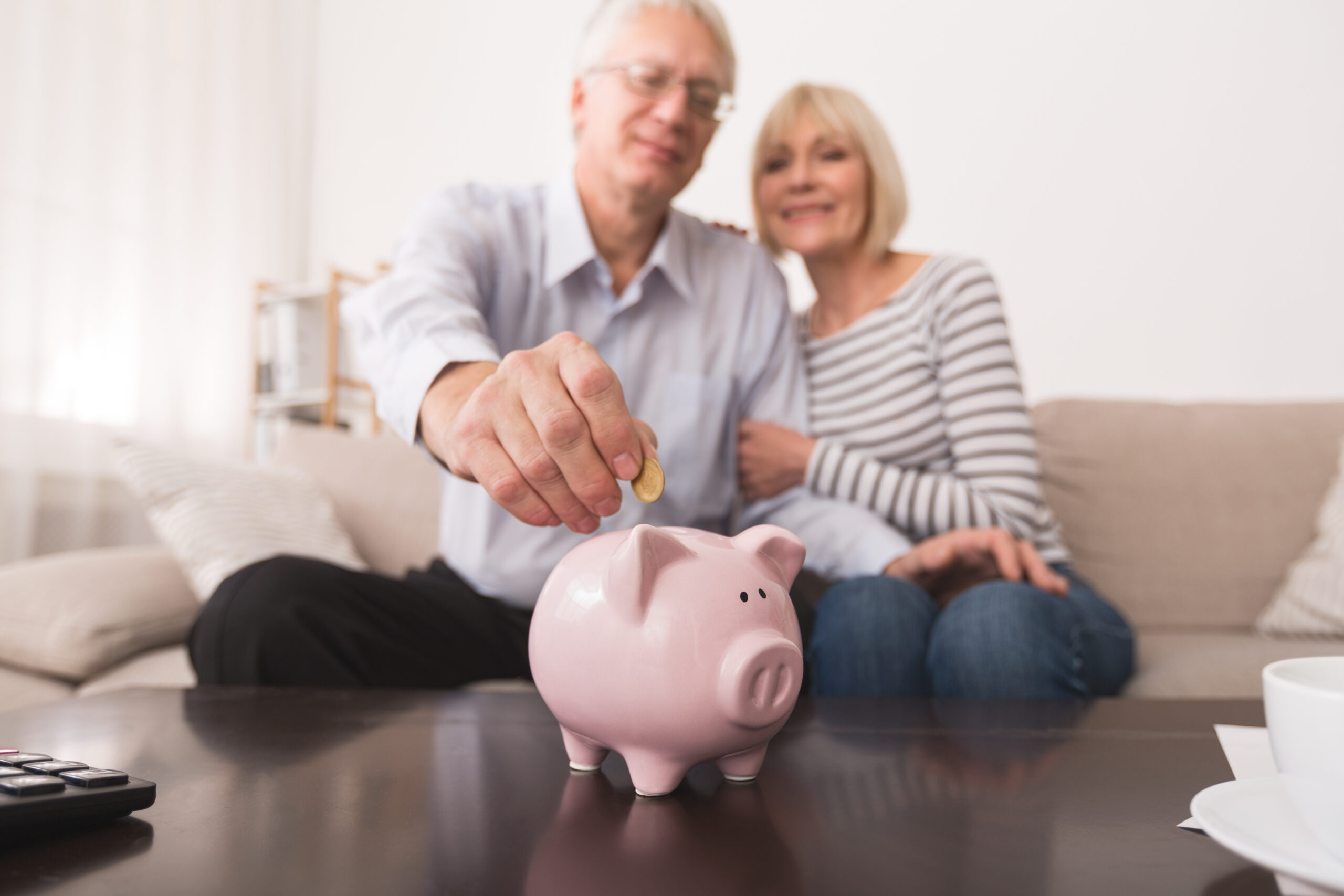 Senior couple putting coin in piggybank, saving money at home